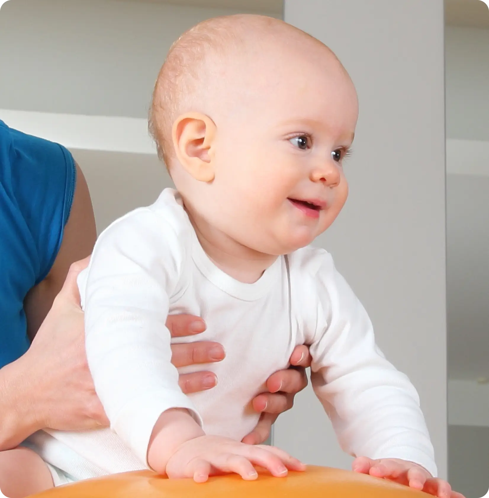 Smiling baby supported by an adult's hands during an early intervention session