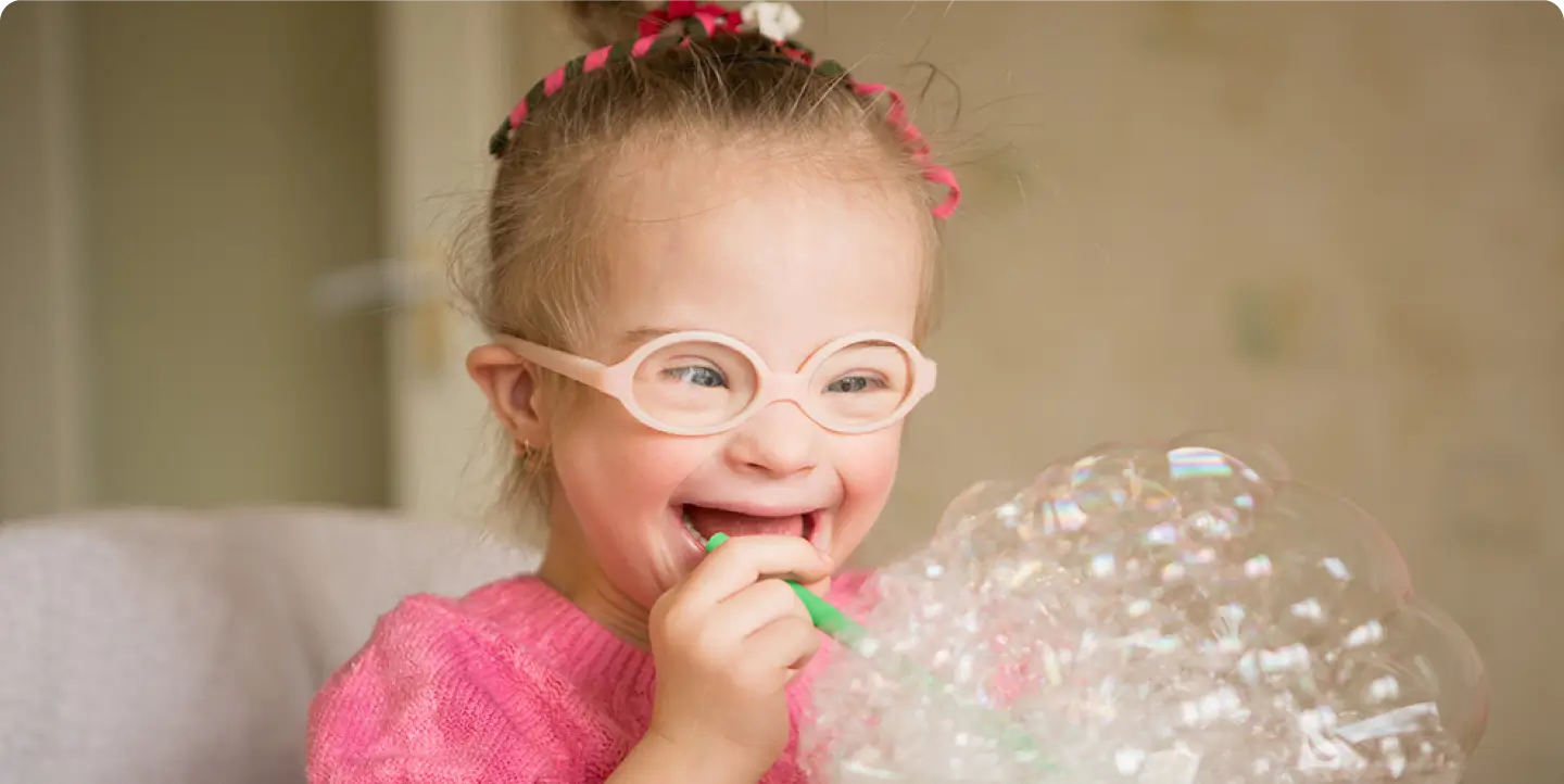 Young child with glasses smiling and playing with bubbles